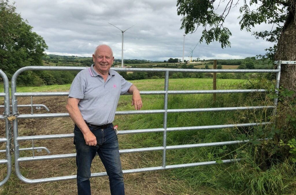 John Sheenan stands in front of his house on the opposite side of the road to demonstrate just how close the wind farm is to his home