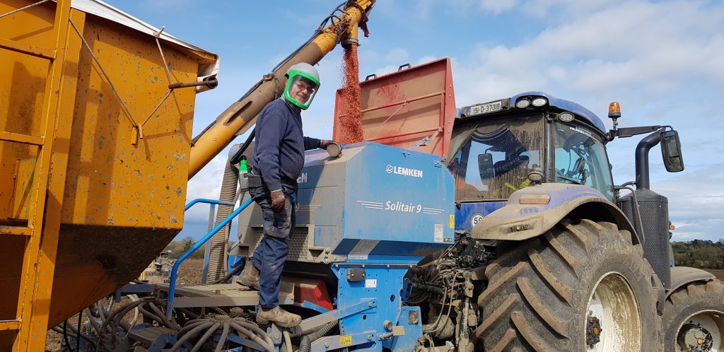Ollie Whyte filling the seed drill wearing a mask which is blowing fresh air at his face and is keeping the dust away
