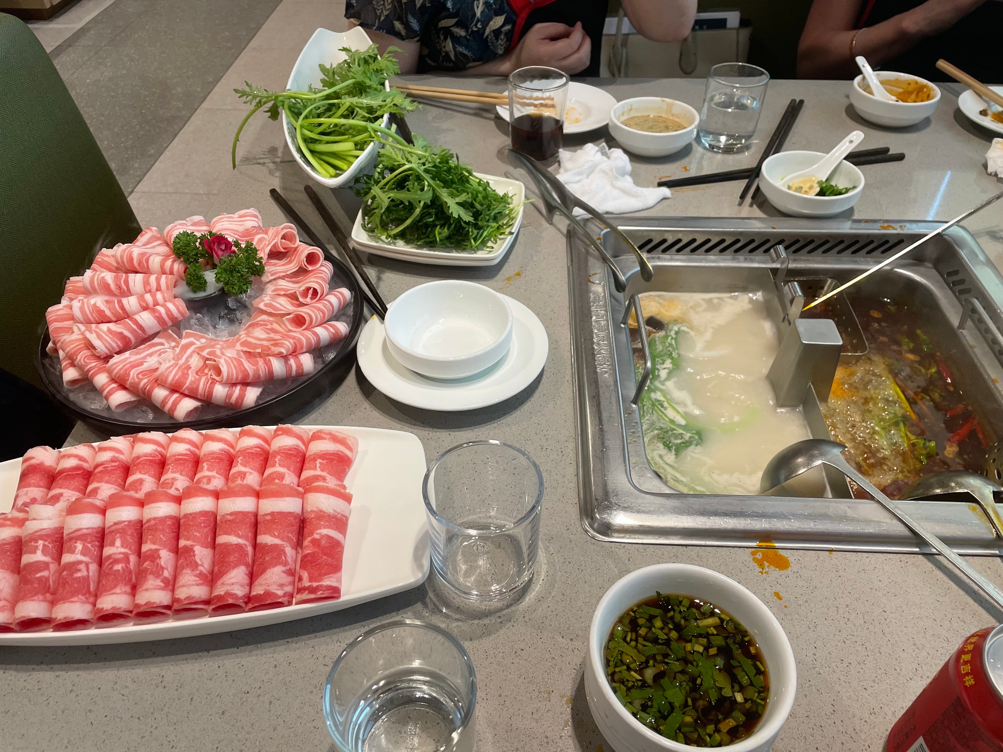 Dining in a typical hotpot restaurant in China. Note the thinly-sliced beef cuts (front) and lamb cuts (rear) which are placed in the hotpot (centre) and then eaten