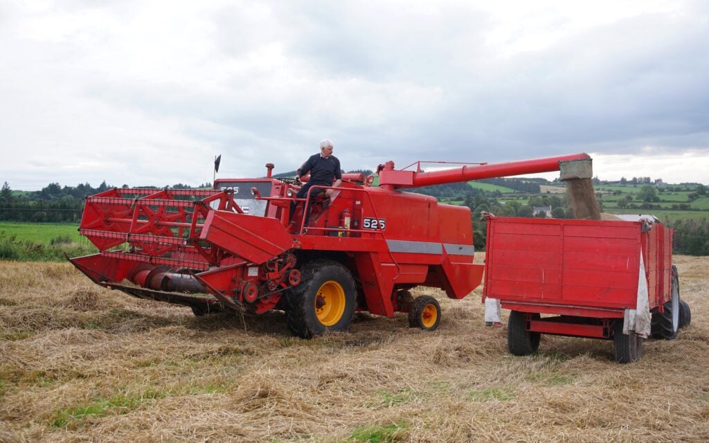The combine's twin tanks are unloaded by horizontal auger into waiting trailer